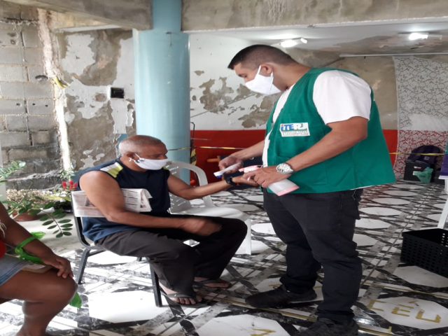 Servidor do ITERJ checando a temperatura corporal e a higienizando a mão de morador de Campo Grande